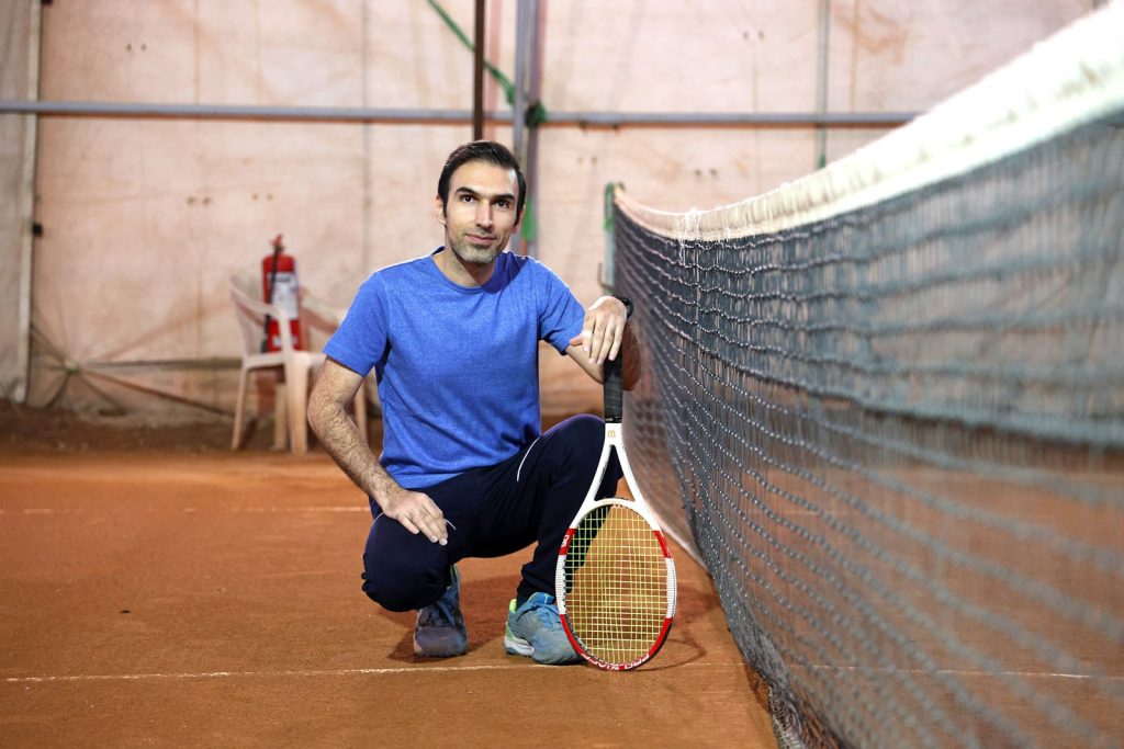 Man with tennis racket on court near net